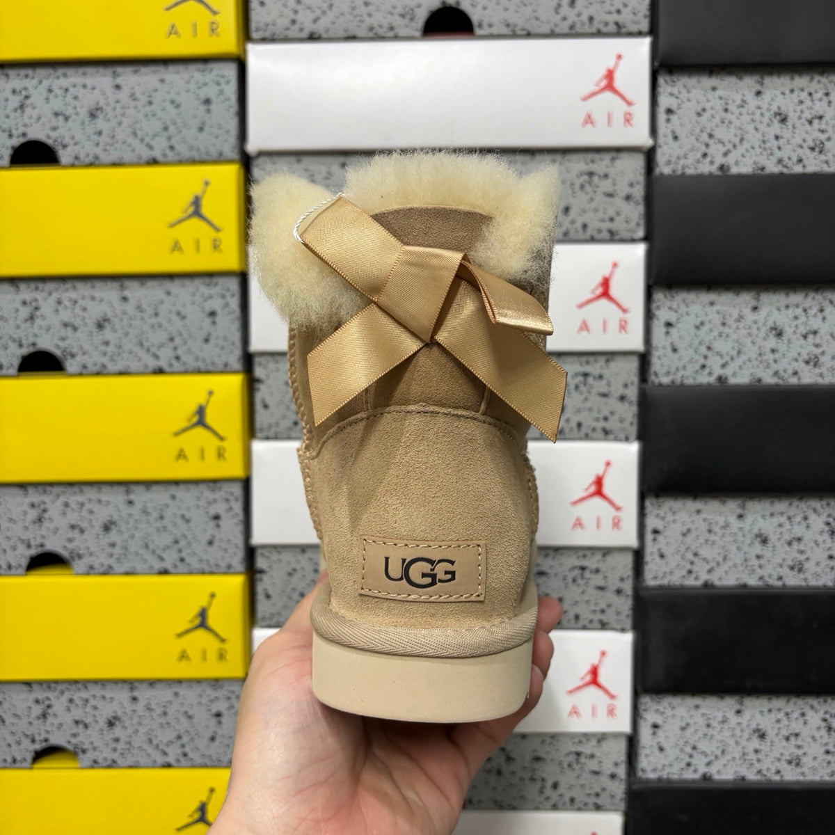 UGG Mini Bailey Bow Ankle Boot – Suede Boot with Cream Shearling Lining, Satin Bow Detail & Sand Sugar Sole in Sand